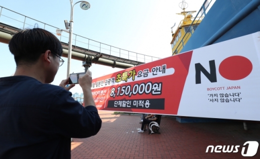 한 시민이 울산시 남구 장생포 고래박물관 앞 광장에 걸린 '8월 일본인 관광객 고래바다여행선 초특가 승선 요금 815만원' 현수막 사진을 찍고 있다. /사진=뉴스1