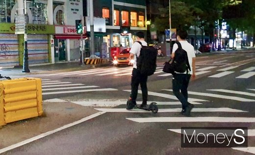 평일 밤 성균관대입구 사거리에서 전동킥보드를 탄 사람이 헬멧을 쓰지 않은 채 횡단보도를 건너고 있다. /사진=홍승우 기자
