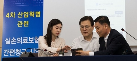 지난해 7월 최종구 전 금융위원장(가운데)이 '실손보험 간편 청구 시연회'에서 스마트폰을 활용해 실손보험금을 직접 청구해보고 있다./사진=금융위원회